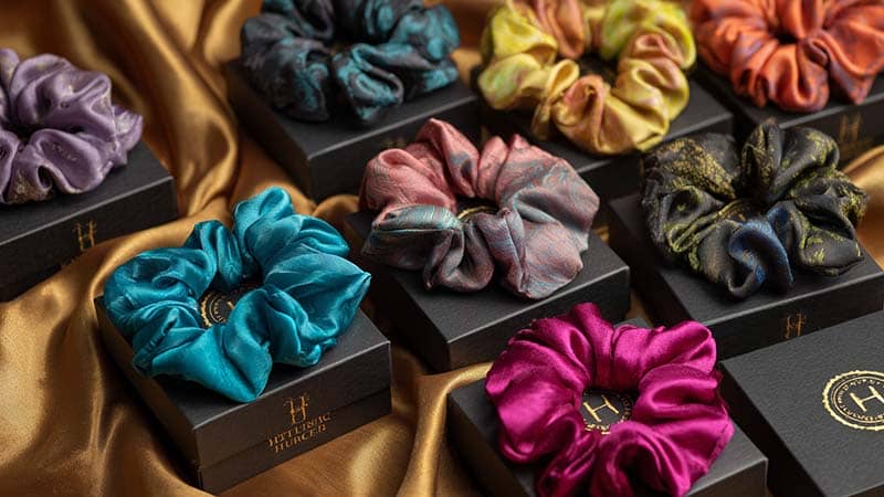 Flat lay of custom silk scrunchies with logo embroidery and colorful packaging boxes