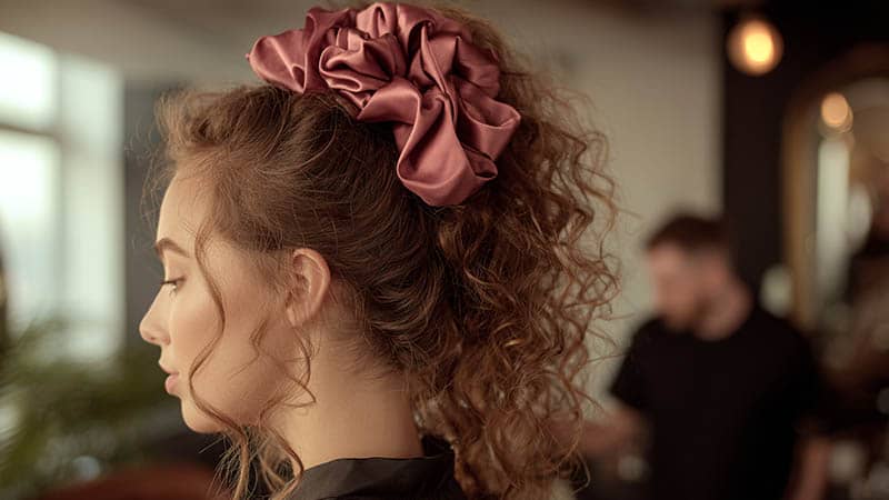 Woman wearing a mulberry silk scrunchie in a modern hair salon, demonstrating silk scrunchies for curly hair and premium styling