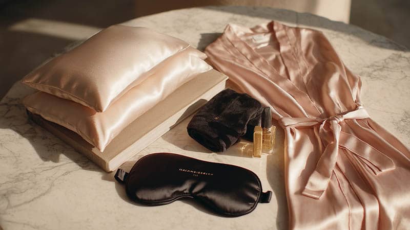 Flat lay of mulberry silk pillowcases, silk bonnets, and a silk sleep mask with luxe robes backdrop, illustrating grade 6A and 22 momme use-cases